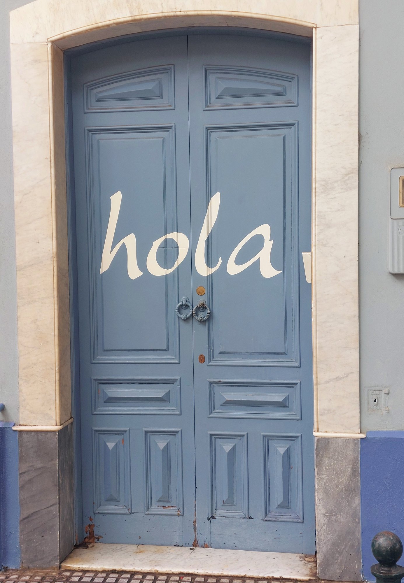 Blaue Tür mit 'hola'-Schriftzug als Straßenkunst in Cádiz
