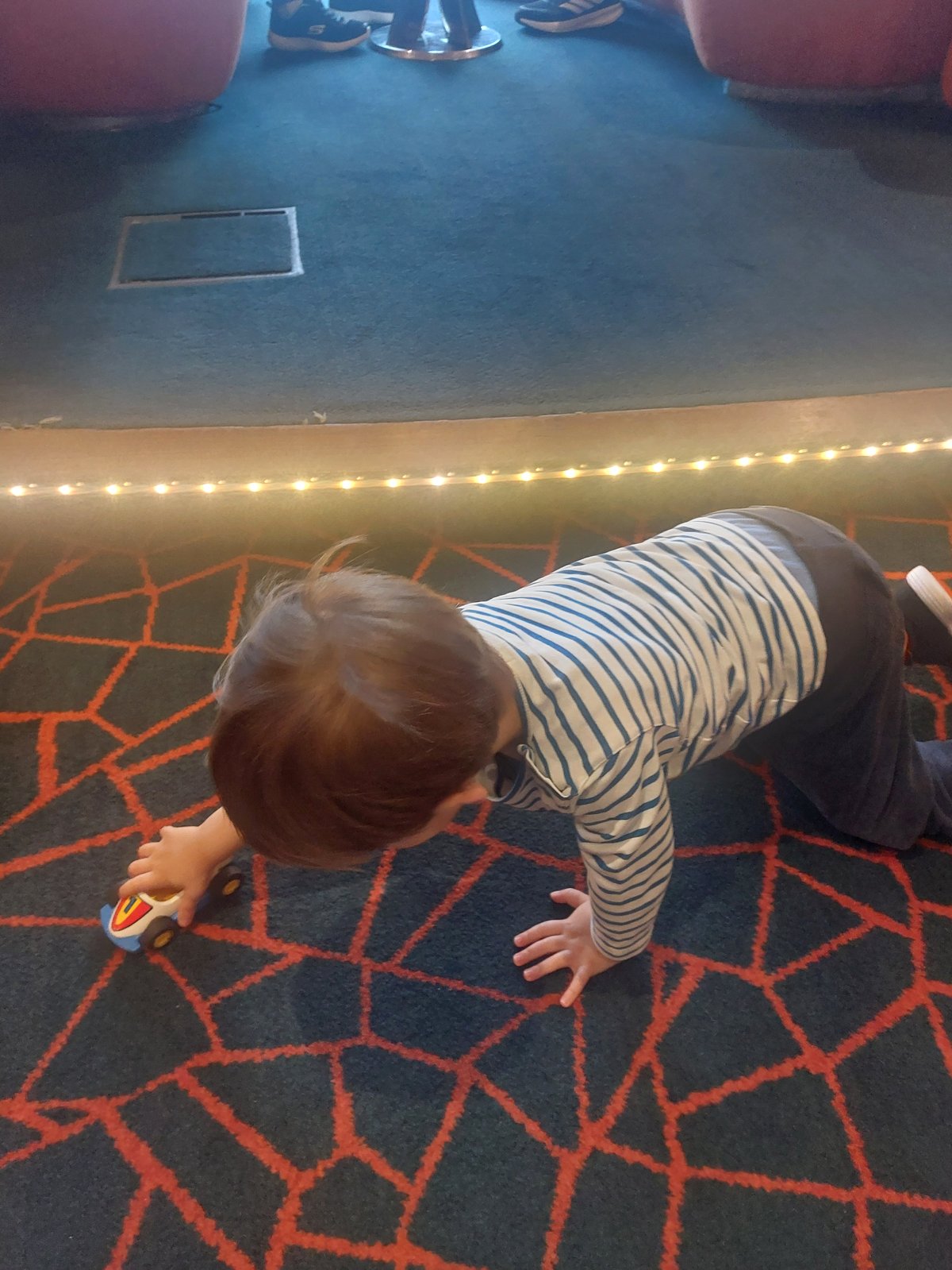 Lolo spielt mit einem Spielzeugauto auf dem Boden während eines Vortrags an Bord